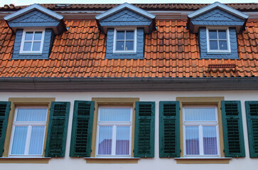 Close-up house. Three windows with green wooden shutters and the smaller windows in the red tile roof. Typical architecture in Bavaria, region Upper Franconia, Germany. Travel and tourism concept