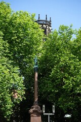 Die Mariens&auml;ule auf dem Marienplatz vor &uuml;ppigem Gr&uuml;n und dem Kirchturm der katholischen Pfarrkirche St. Ludgeri im Sommer bei blauem Himmel und Sonnenschein in M&uuml;nster in Westfalen im M&uuml;nsterland