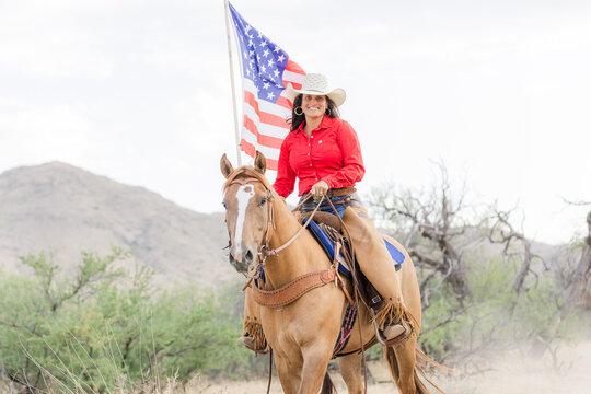 Cowgirl riding her Mustang horse carrying US flag
