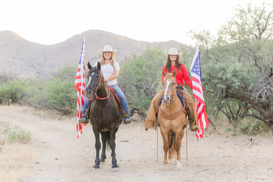 Cowgirls on their Mustang horses in the Arizona desert carrying US flags