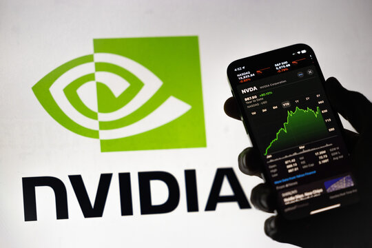 Porto, Portugal - April 30, 2024: A backlit hand holds a phone, showcasing green ascending Nvidia stock prices within the Apple stock market app. In the backdrop, a blurred screen of the logo