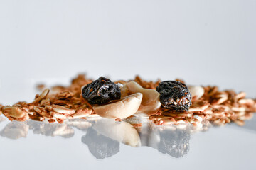 Stack of granola with pieces of peanuts and raisins. White background and glass reflection.