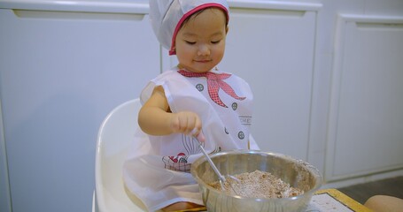 Adorable Toddler child Chef Mixing Ingredients in a Bowl, showcasing culinary skills making sweet...
