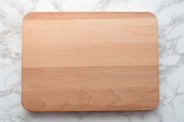 A beech wood cutting board pictured from above. White-and gray marble background
