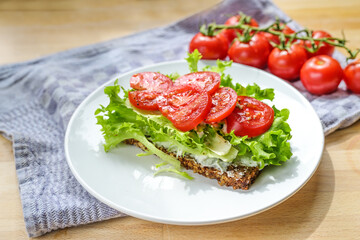 Tomato and lettuce on a slice of wholegrain bread, healthy sandwich on a white plate, blue kitchen...