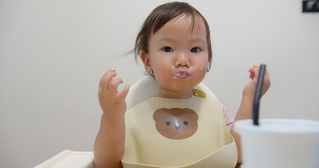 Cute Adorable toddler enjoying Eating a snack in a high chair wearing a bib with a bear design in a...