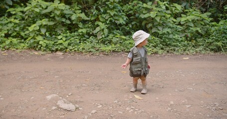 Cute Adorable toddler child girl wearing a safari outfit and hat standing on a dirt path in a lush green forest looking curious and adventurous Exploring Nature Surrounded by Lush Greenery © HarryKiiM Stock