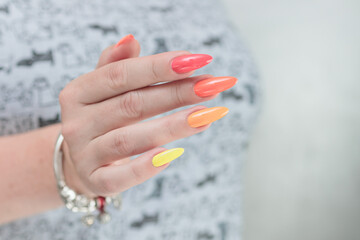 Multicolored manicure, female hands with colored nails, nail polishes, yellow, orange and pink colors.