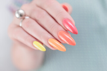 Multicolored manicure, female hands with colored nails, nail polishes, yellow, orange and pink colors.