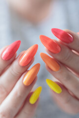 Multicolored manicure, female hands with colored nails, nail polishes, yellow, orange and pink colors.