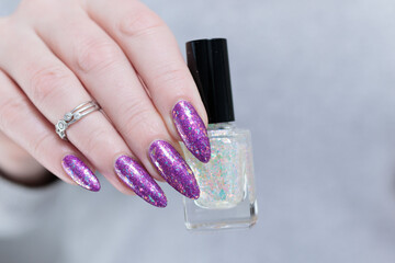 Woman hand with long nails and a bottle of bright purple nail polish