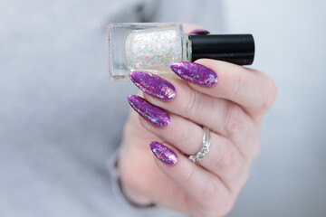 Woman hand with long nails and a bottle of plum purple nail polish