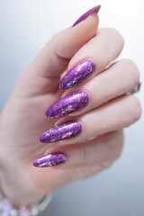 Woman hand with long nails and a bottle of bright purple nail polish