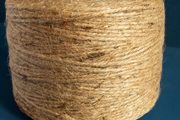 Close up of  a spool of natural fiber twine against a dark blue background highlights the intricate texture and pattern of the twine. pPackaging, rustic decor and natural materials.