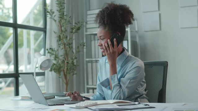 Confident african american businesswoman multitasking with laptop and phone in modern office. Slow motion captures her focused work in detail