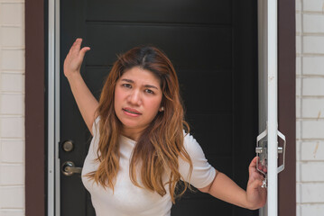 An angry asian woman in her 30s stands just outside her apartment flat, looking livid and...