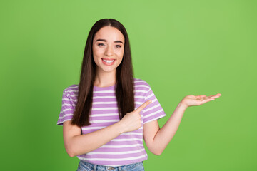 Photo portrait of lovely young lady point hold empty space dressed stylish striped violet garment isolated on green color background