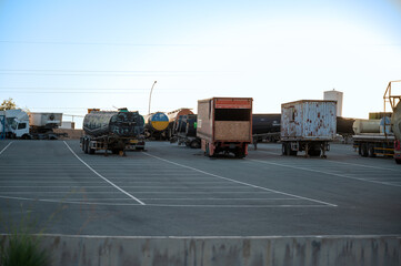 Various types of trucks parked in a large parking area, with assorted truck parts.
