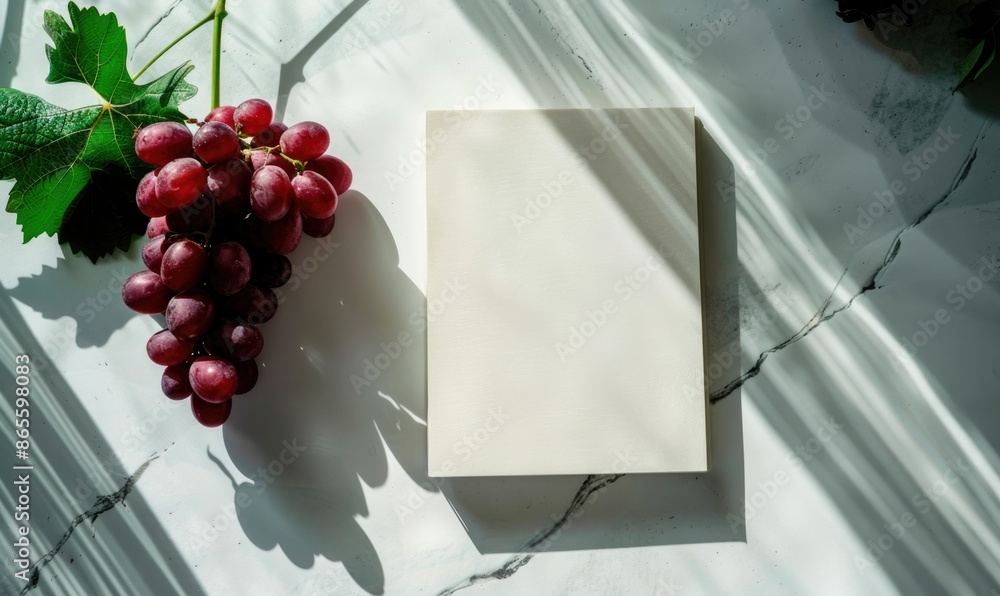 Poster closed notebook on a white table with a bunch of grapes