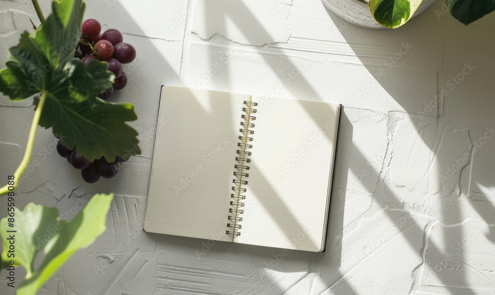 Poster closed notebook on a white table with a bunch of grapes