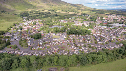 Low level aerial footage over the rural village of Lennoxtown in Central Scotland with village pond and range of hills in background.
