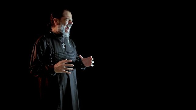 SINGER WITH LONG BEARD DRESSED IN BLACK ROOM SINGING ON A BLACK BACKGROUND
