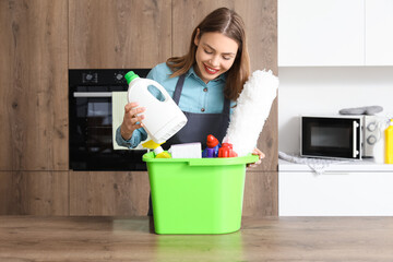 Young woman with cleaning supplies at table in kitchen