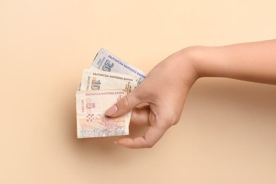 Female hand holding Bulgarian lev banknotes on beige background