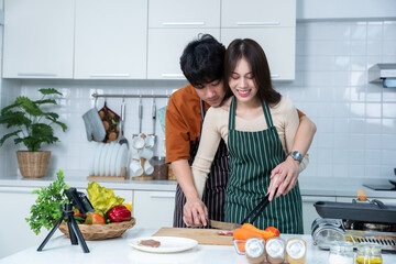 Happy portrait of loving young asian of having fun standing a cheerful preparing food and enjoy cook cooking with vegetables, meat, bread while standing on a kitchen Condo life or home