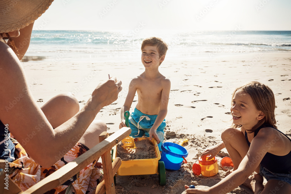 Poster Mother, children and sandcastle at beach, happy and vacation in summer, playful or container for bonding. Mom, boy and girl in family, holiday and toys with bucket, sunshine or sea with cart for game