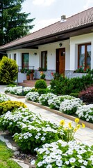 A white house with a brown roof and a brick driveway is surrounded by lush green landscaping