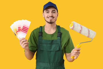 Young painter with color palettes and roller on yellow background