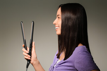 Obraz premium Beautiful young woman with hair straightener on light background
