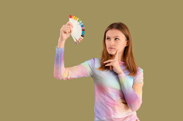 Thoughtful young woman with nail polishes palette on green background