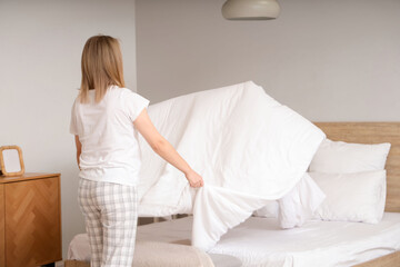 Young woman making bed in bedroom, back view