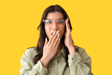 Surprised young woman in eyeglasses on yellow background