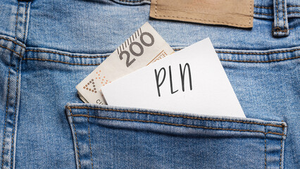 White card with a handwritten inscription "PLN", put into the pocket of blue pants jeasnow, next to Polish banknotes PLN (selective focus)