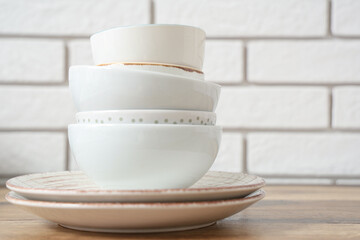 Stack of clean tableware on wooden table near white brick wall