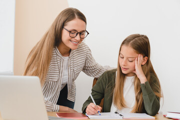 Young female tutor teacher babysitter nanny mother helping her daughter student pupil schoolgirl...