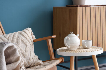 Stylish interior of blue living room with soft armchair, chest of drawers and coffee table