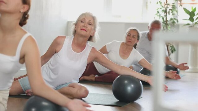 A group of elderly amateurs with a girl instructor perform a simplified exercise with a soft ball - Eka -Pad - Rajakapotasanawith a side slope