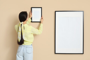 Young woman hanging picture frame on beige wall in room