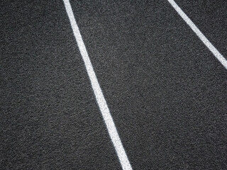 Track and Field Running Lanes. Overhead view of a rubber black running track surface with white lane lines. Surface level view of the textured artificial black surface. There is a slight curve. 