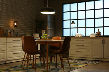 Interior of kitchen with glowing lamps, white counters, oven, table and chairs at evening