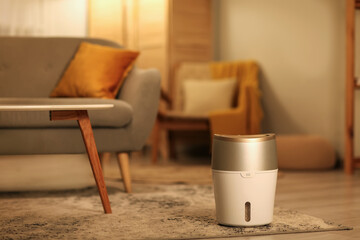 Modern humidifier near sofa on floor in living room at evening