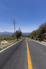 road in the middle of the hill with trees on each side, and a natural stone wall on one side with a completely blue sky