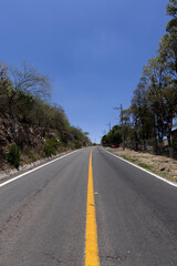 Fototapeta premium road in the middle of the hill with trees on each side, and a natural stone wall on one side with a completely blue sky