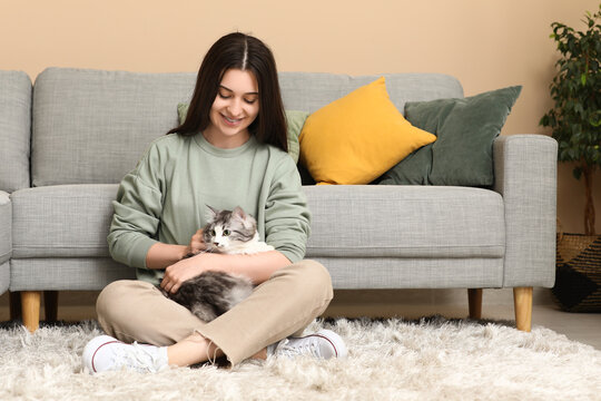 Young woman with cute longhaired cat sitting on floor in living room