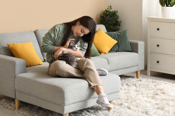 Young woman pet her cute longhaired cat and sitting on sofa in living room