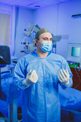 A doctor in a surgical suit is standing in the operating room. A doctor in gloves and a gown prepares for eye surgery using a modern microscope